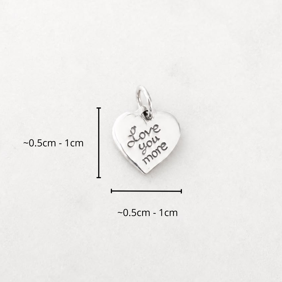 Small sterling silver heart charm engraved with Love You More, shown with a 0.5cm to 1cm size guide